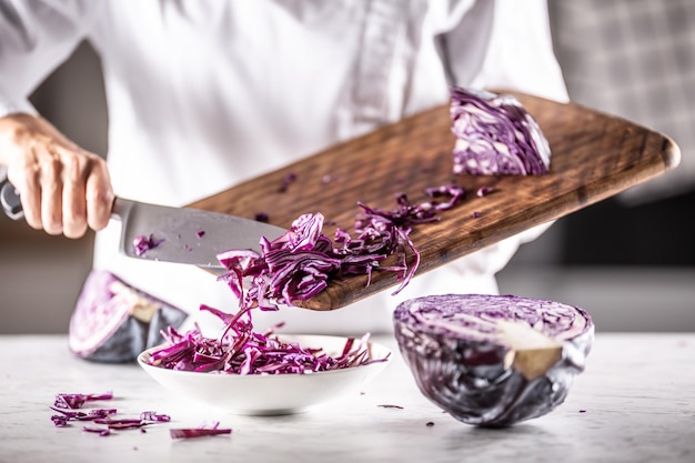 El chef corta la mitad de una col roja cruda en trozos y los pone en un tazón.