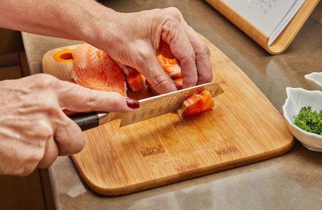 Chef corta o salmão em cubos com faca para preparar o prato de acordo com a receita