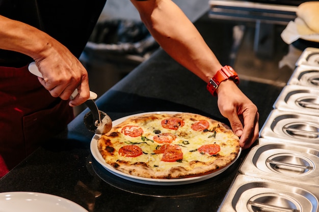 El chef corta una pizza caliente de Caprese Bianca antes de servirla. Los ingredientes son Mozzarella