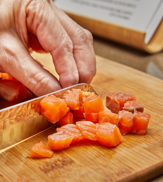 Chef corta el salmón en cubos con un cuchillo para preparar el plato según la receta