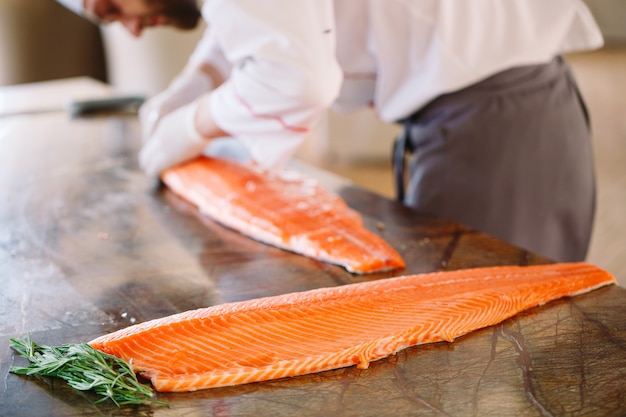 El chef corta el salmón sobre la mesa.