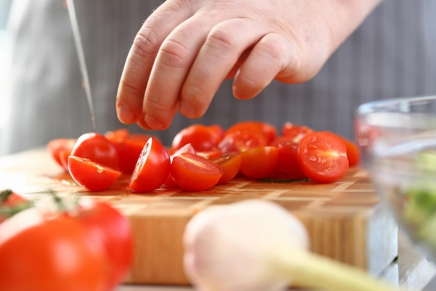 El chef corta tomates maduros frescos en una tabla de cortar rodeada de ingredientes