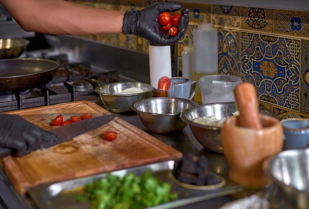 El chef corta los tomates, prepara los ingredientes para el plato en la mesa de la cocina.