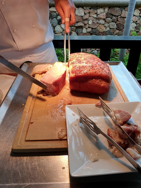 Chef cortando carne jamón de cerdo sirvió a los huéspedes a la hora del desayuno en el restaurante del hotel