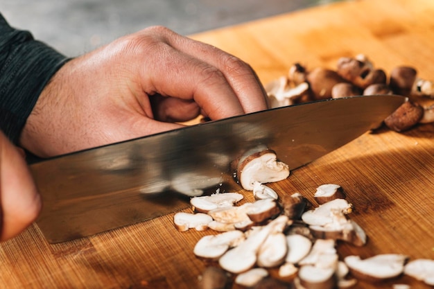 Chef cortando champiñones shiitake con un cuchillo en una tabla de cortar de madera