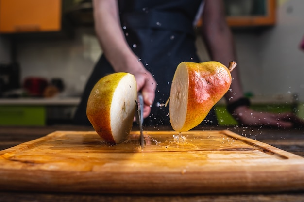 Chef cortando una pera madura amarilla por la mitad con un cuchillo grande en movimiento