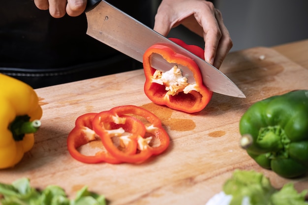 Foto chef cortando pimiento dulce en rodajas en la tabla de cortar de madera en la cocina