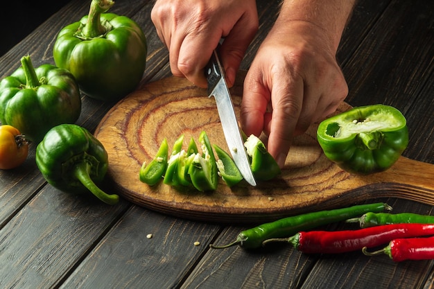 El chef cortando pimientos verdes frescos en una tabla para cortar madera