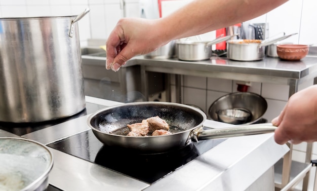 Chef cozinha batatas fritas com pedaços de carne em uma cozinha de restaurante