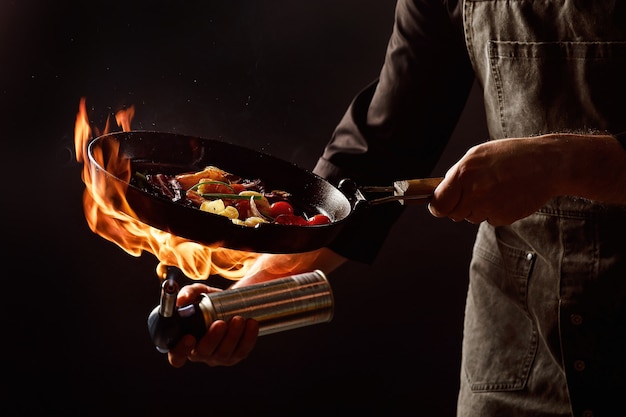 Chef cozinha com fogo em uma panela de camarão com legumes