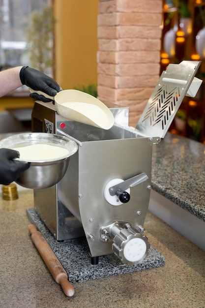 Chef cozinha espaguete italiano usando uma máquina de macarrãoEle despeja farinha e sêmola em uma máquina de macarrão