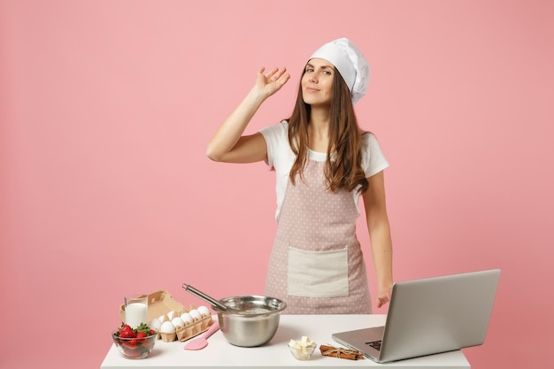 Chef cozinheiro confeiteiro ou padeiro em camiseta branca de avental, chapéu de chefs de toque cozinhando bolo de natal ou laptop de pc cupcake na mesa isolada em fundo rosa pastel. conceito de simulação. mostrando gesto bem.