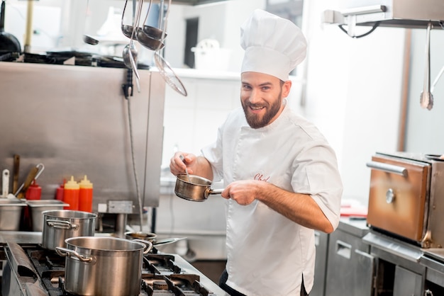 Chef cozinheiro uniformizado, cozinhando sopa no grande fogão da cozinha do restaurante