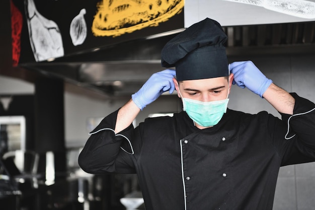 chef cozinheiro usando máscara médica protetora facial para proteção contra a doença do vírus corona com prato de sanduíche autêntico na cozinha profissional do restaurante. Conceito de saúde, segurança e pandemia em novo