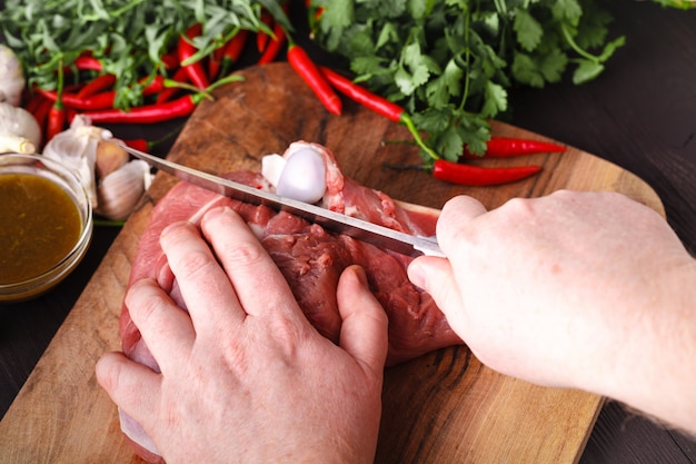 Chef con un cuchillo en la mano corta carne fresca en una mesa