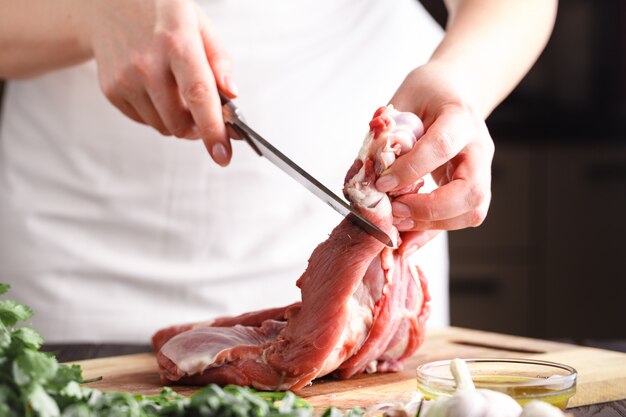 Chef con un cuchillo en la mano corta carne fresca en una mesa