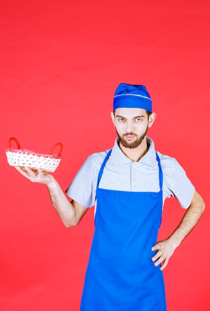 Chef de avental azul segurando uma cesta de pão coberta com uma toalha vermelha.