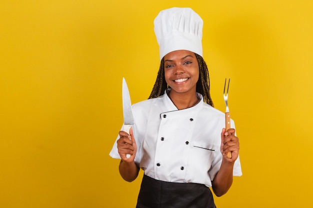 Chef de cozinha afro-brasileira jovem segurando faca e garfo para churrasco se preparando para cozinhar