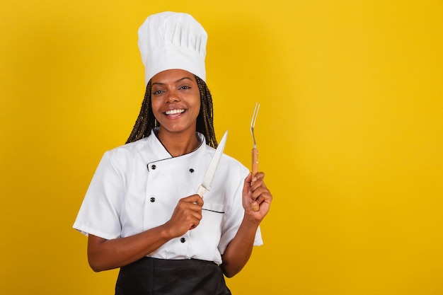 Chef de cozinha afro-brasileira jovem segurando faca e garfo para churrasco se preparando para cozinhar