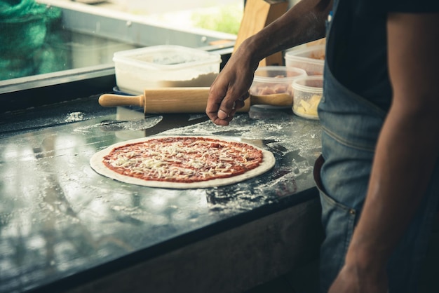 Chef de mão preparando queijo espalhado na pizza na mesa de mármore closeup fazendo pizza