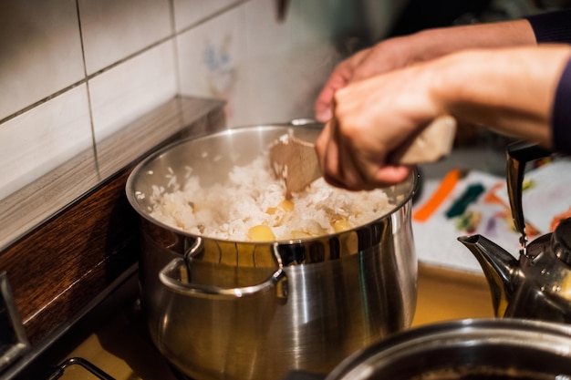 Chef de mão usando nadadeira de madeira misturando arroz com batata na panela