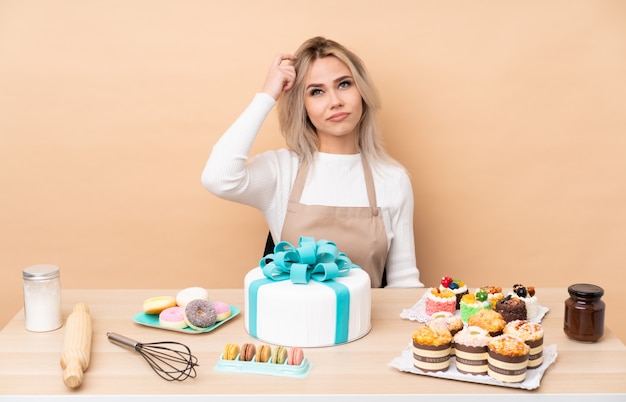 Chef de pastelaria adolescente com um bolo grande em uma mesa com dúvidas e com a expressão do rosto confuso