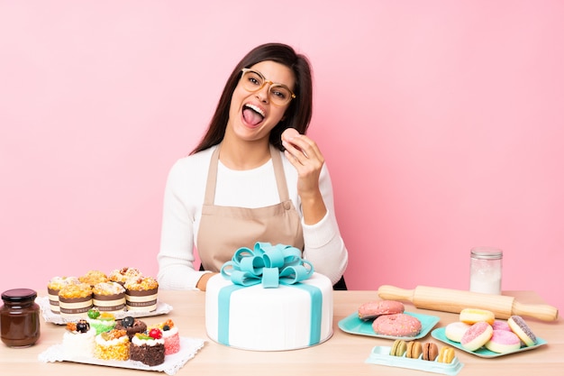 Chef de pastelaria com um bolo grande em uma mesa na parede rosa