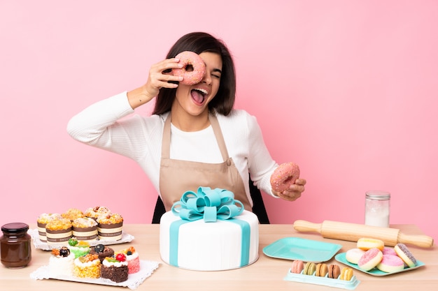 Chef de pastelaria com um bolo grande em uma mesa sobre parede rosa isolada