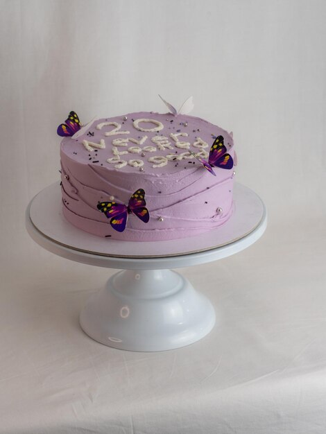 Chef de pastelaria decorando um bolo de aniversário fosco roxo com cobertura de texto polvilha pérolas e borboletas