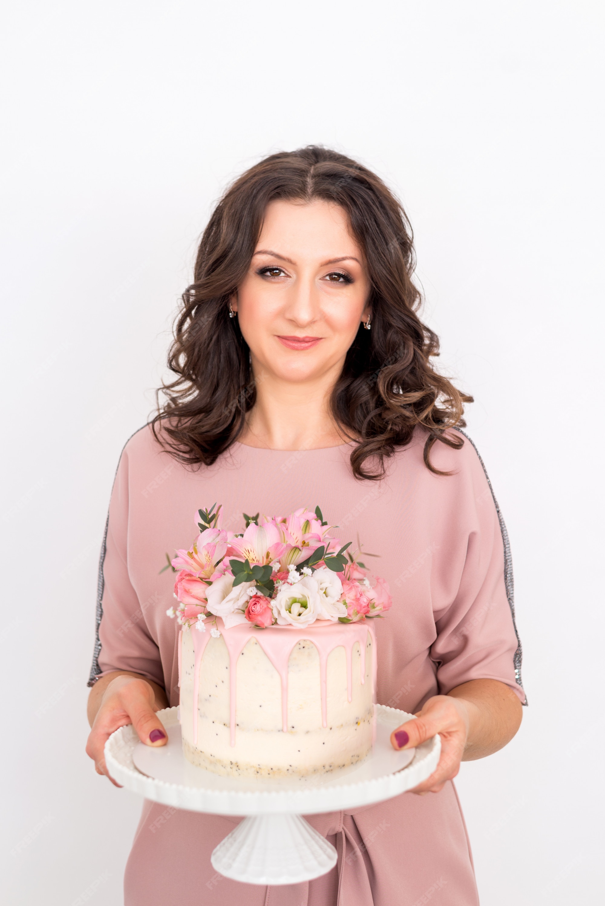 Chef de pastelaria feminino mantém um bolo decorado com flores sobre fundo  branco