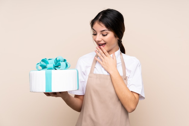 Chef de pastelaria mulher segurando um bolo grande com surpresa e expressão facial chocado