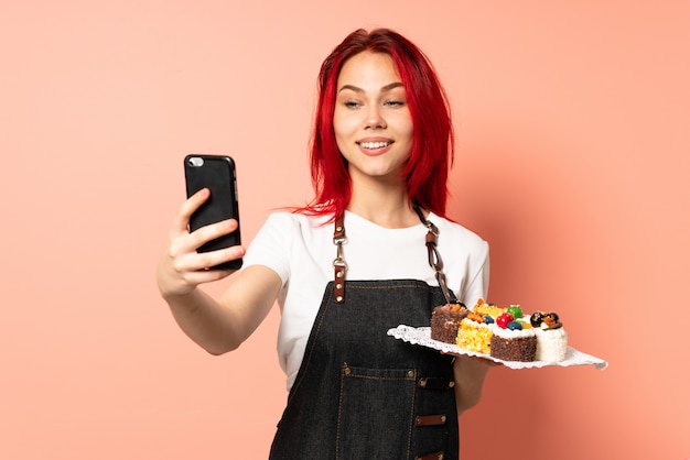 Foto chef de pastelaria segurando um muffins isolado na parede rosa, fazendo um selfie