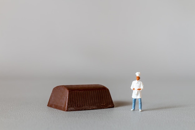 Chef de pessoas em miniatura com pé de chocolate em pé contra um fundo cinza