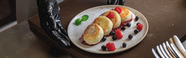 El chef decoró tartas de queso con crema de bayas y azúcar en polvo para desayunar en la cocina del restaurante