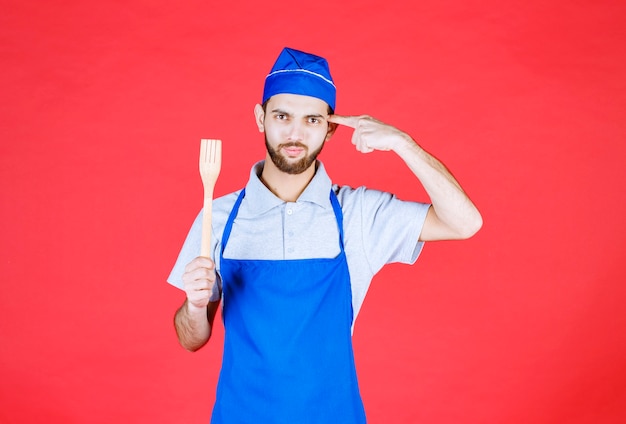 Chef en delantal azul sosteniendo una espátula de madera y teniendo una buena idea.