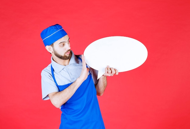 Chef en delantal azul sosteniendo un tablero de información ovale.