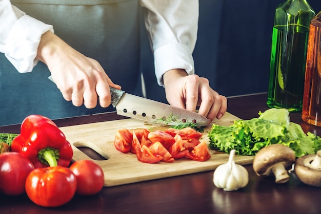 Chef en delantal negro cortando verduras