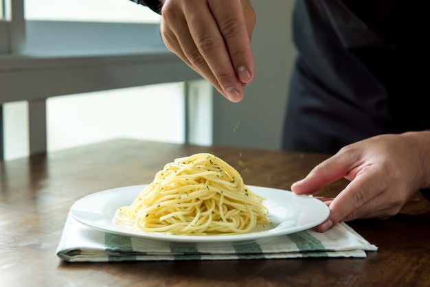 Chef, der italienische Spaghettis mit Grundpetersilie würzt