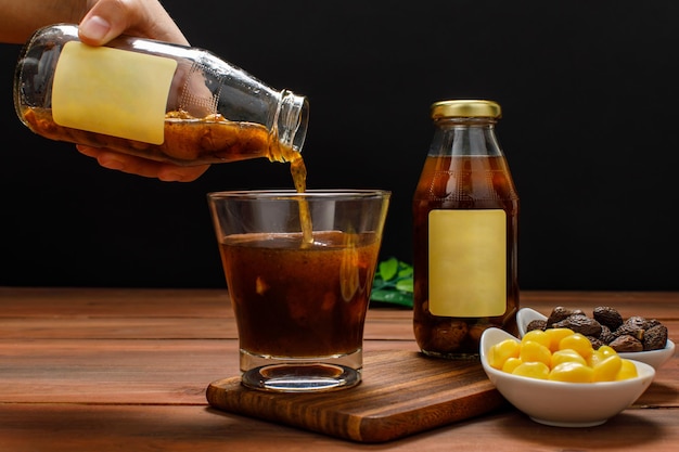 Chef derramando bebida de extrato de fruta da garrafa de vidro no copo na mesa de jantar com uma tigela de ginkgo orgânico natural e noz de malva. A bebida publicitária servia como sobremesa doce para nutrição saudável.