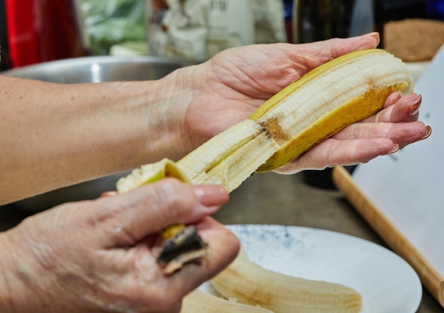 Chef descascado banana para fazer torta na cozinha de casa.