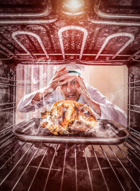 Chef divertido pasó por alto el pollo asado en el horno, por lo que había quemado, vista desde el interior del horno. Cook perplejo y enojado. ¡El perdedor es el destino!