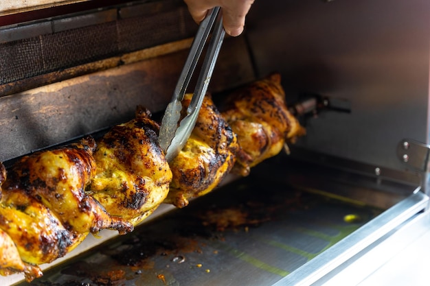 Chef do restaurante kebab com uma ferramenta de metal controlando a grelha de frango