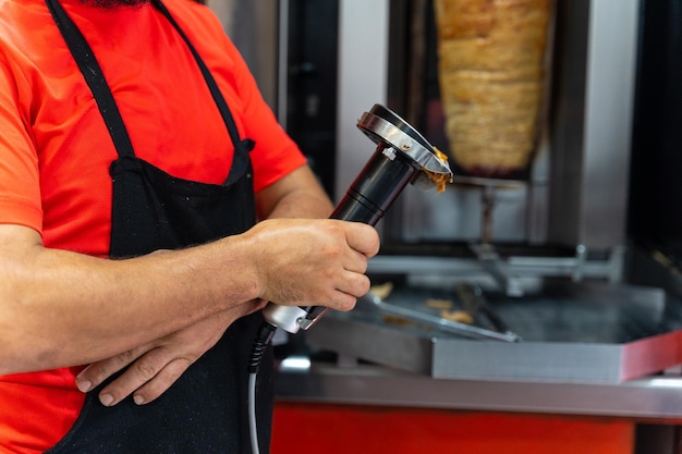 Chef do restaurante kebab usando a ferramenta elétrica para cortar carne doner da grelha