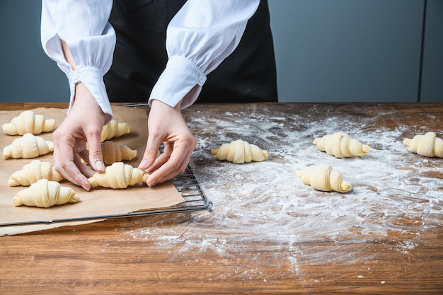 El chef elabora manualmente croissants en la mesa con los ingredientes.