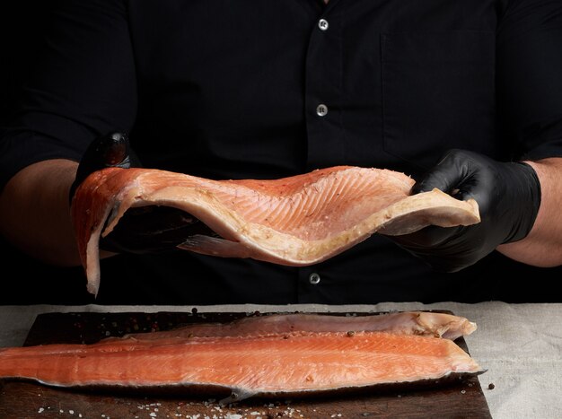 Chef em uma camisa preta e luvas de látex pretas detém um grande pedaço de filé de peixe salmão