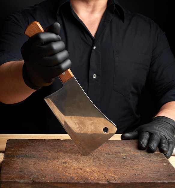 Foto chef em uma camisa preta e luvas de látex pretas segura uma faca de cozinha grande