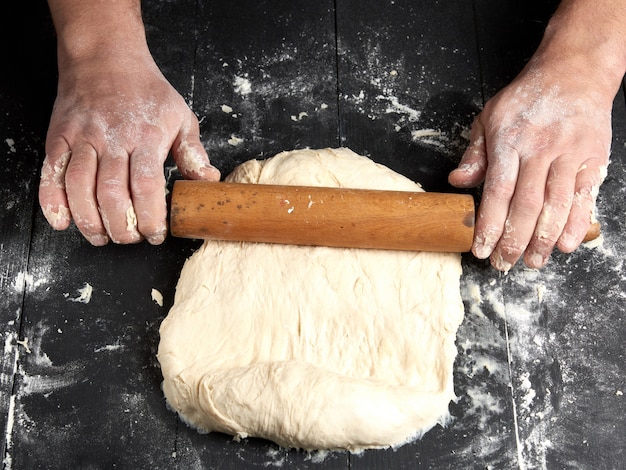 Chef em uma túnica preta rola uma massa para uma pizza redonda