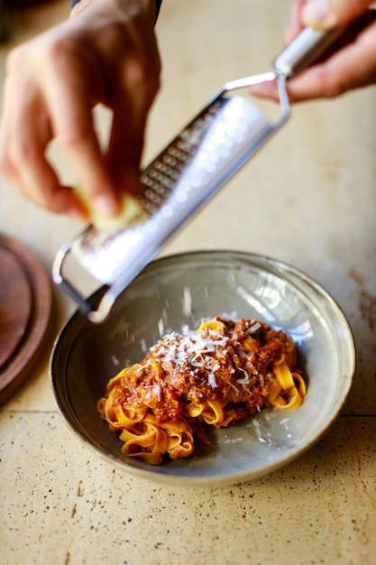 Chef esfrega parmesão em um prato de macarrão com molho à bolonhesa