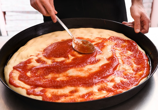 Chef esparciendo pasta de tomate sobre una base de pizza