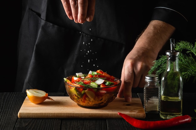 Chef espolvorea ensalada de verduras frescas saladas en un plato sobre una mesa de madera